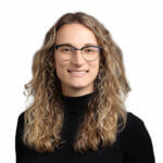 Woman with wavy brown hair and glasses wearing a black top, smiling at camera