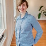 Woman wearing light blue denim shirt standing indoors with hands on hips