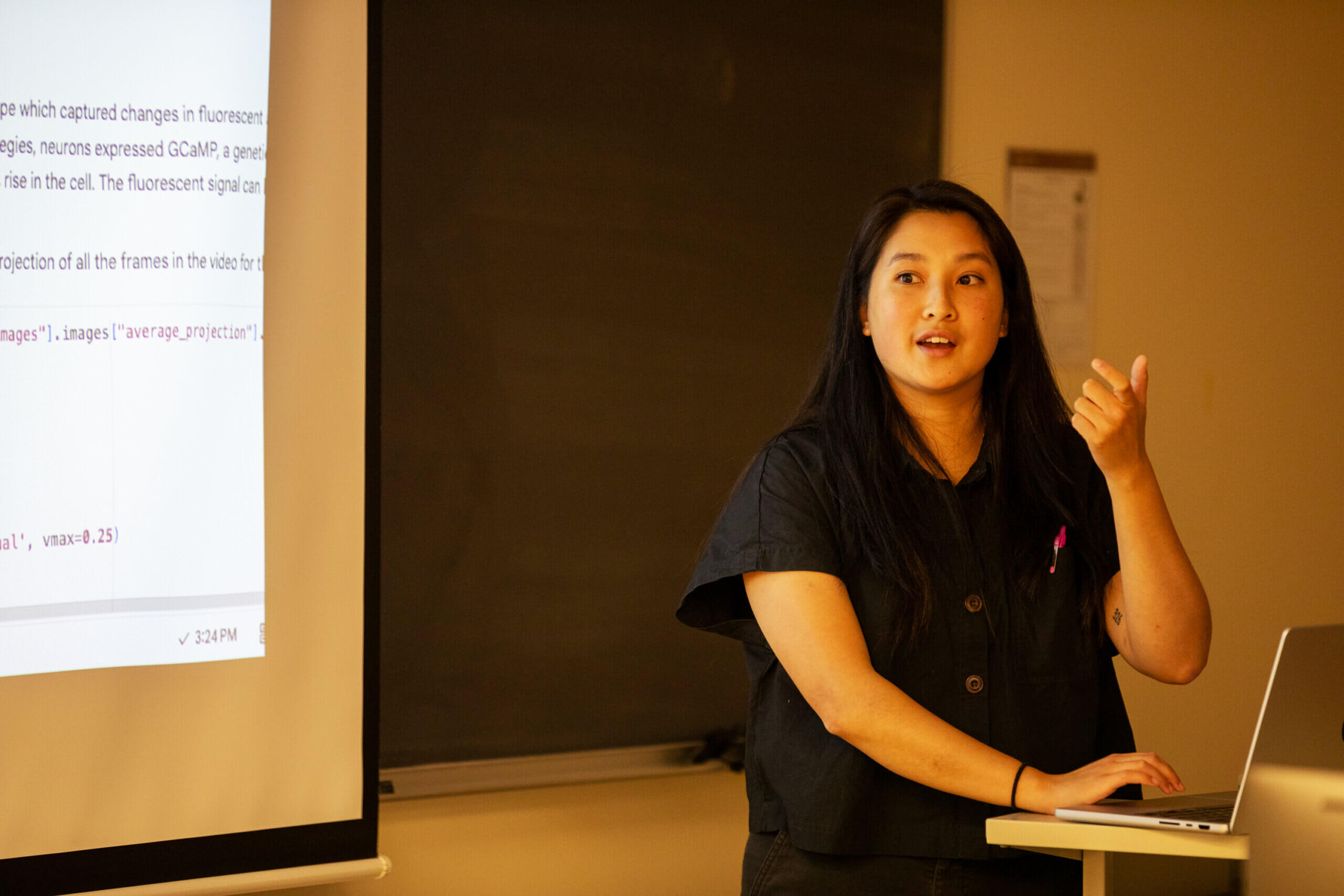 Woman giving presentation about fluorescent imaging, gesturing while standing near laptop and projection screen