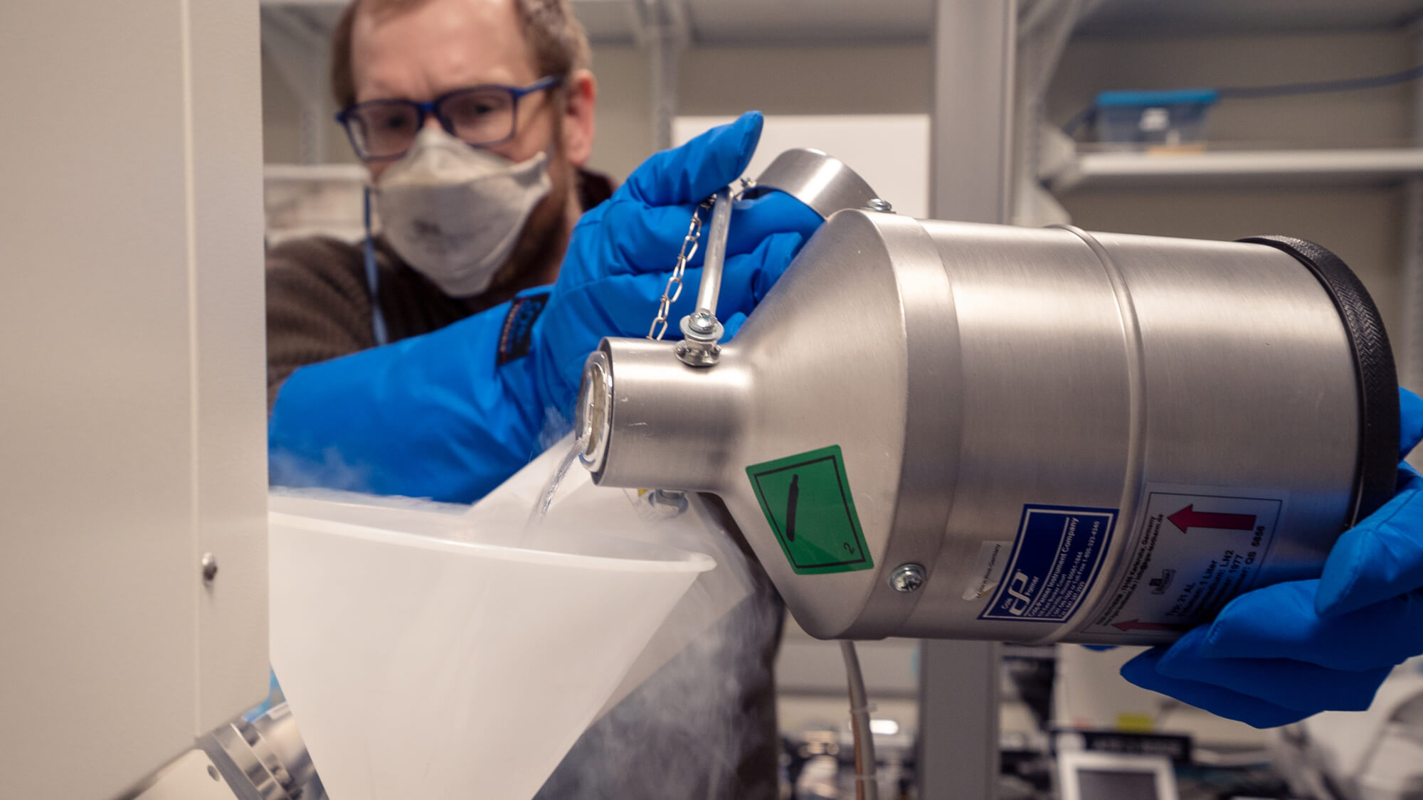 Person in blue gloves and mask examining metallic laboratory equipment in clean room