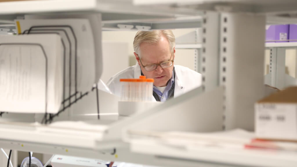 Scientist in white lab coat examines samples in modern laboratory setting with equipment