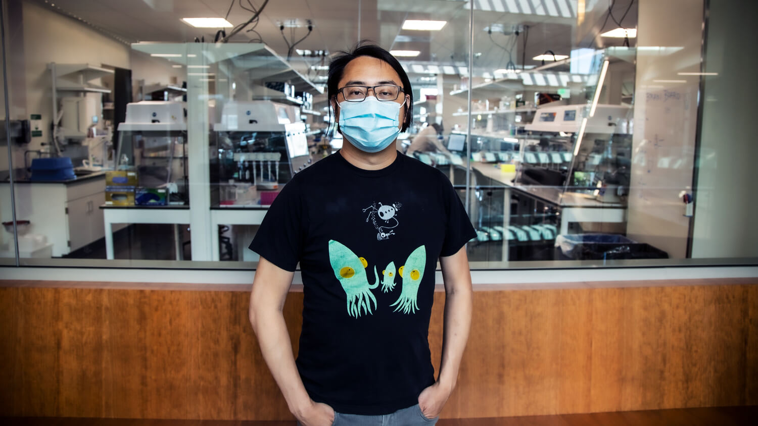 Person wearing glasses and blue mask in laboratory with scientific equipment
