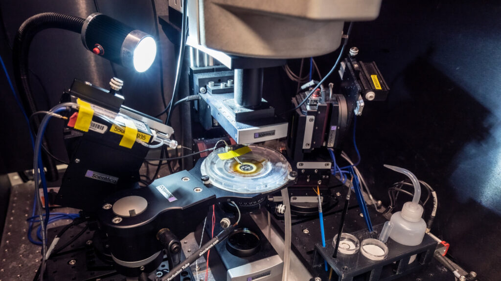 Scientific laboratory equipment with bright lights, mirrors, and electrical components on dark surface.