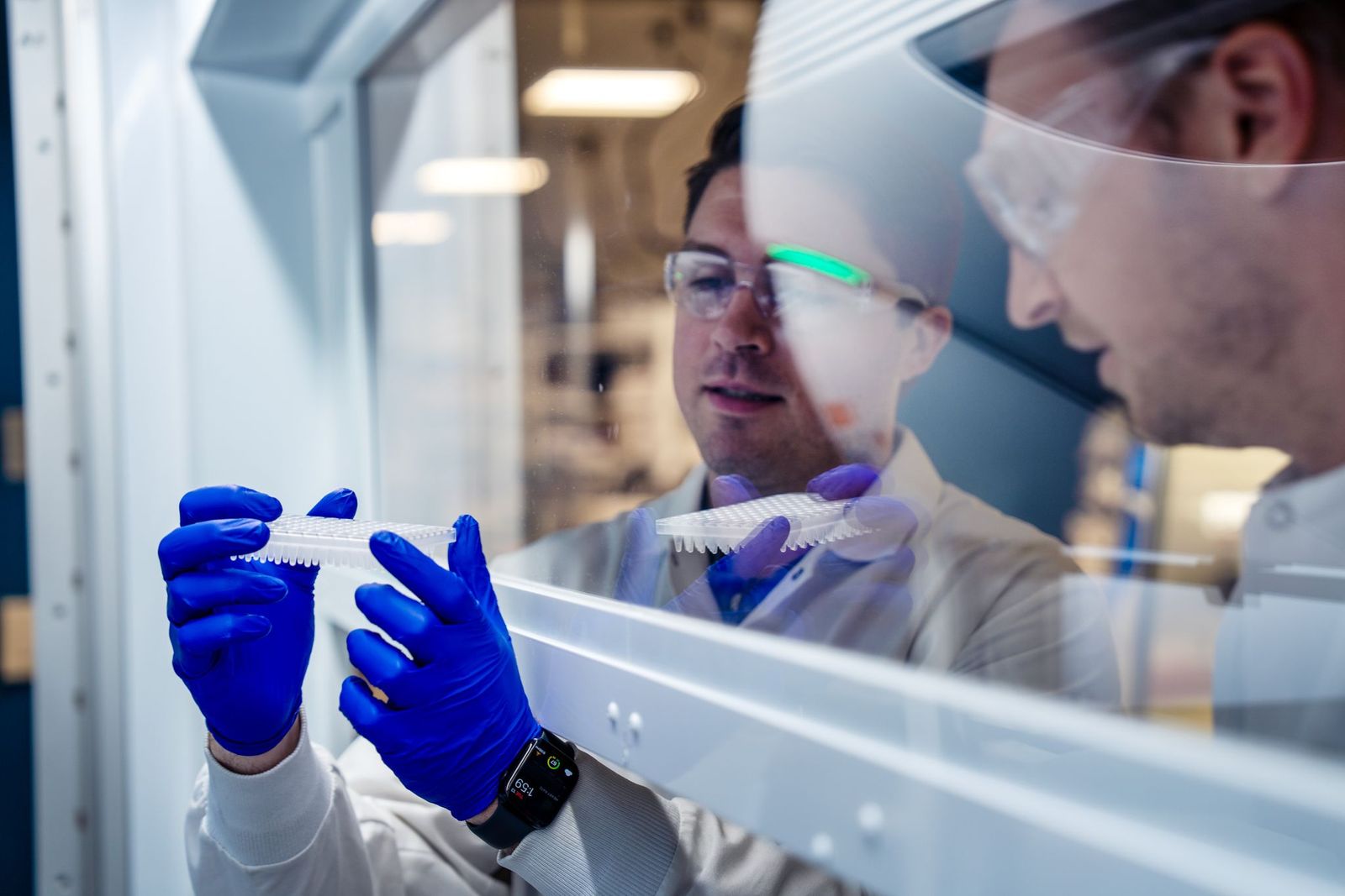 Scientists in lab coats and blue gloves examine samples in modern laboratory with equipment