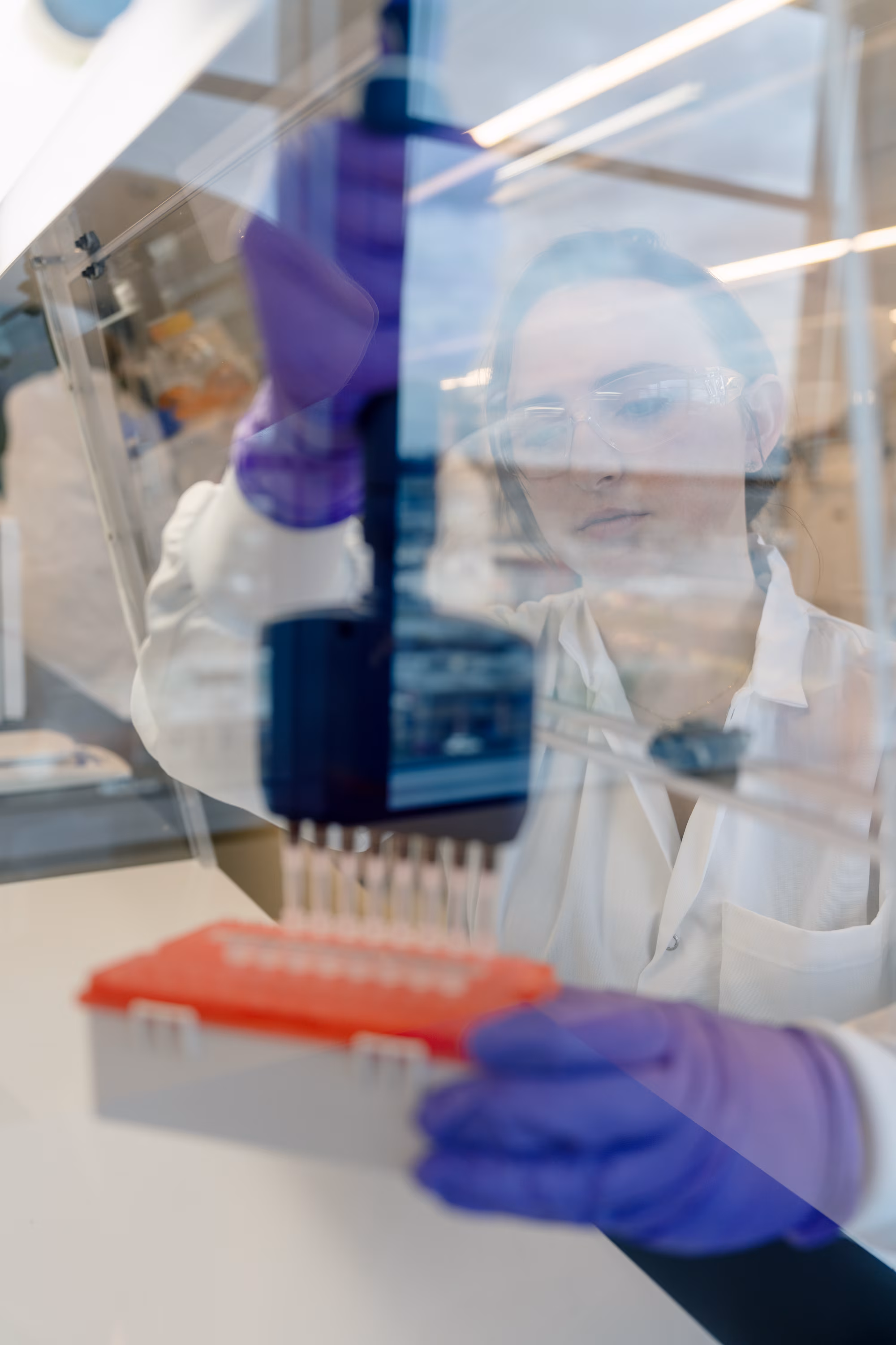 Scientist in white lab coat using purple pipette in bright laboratory setting with equipment