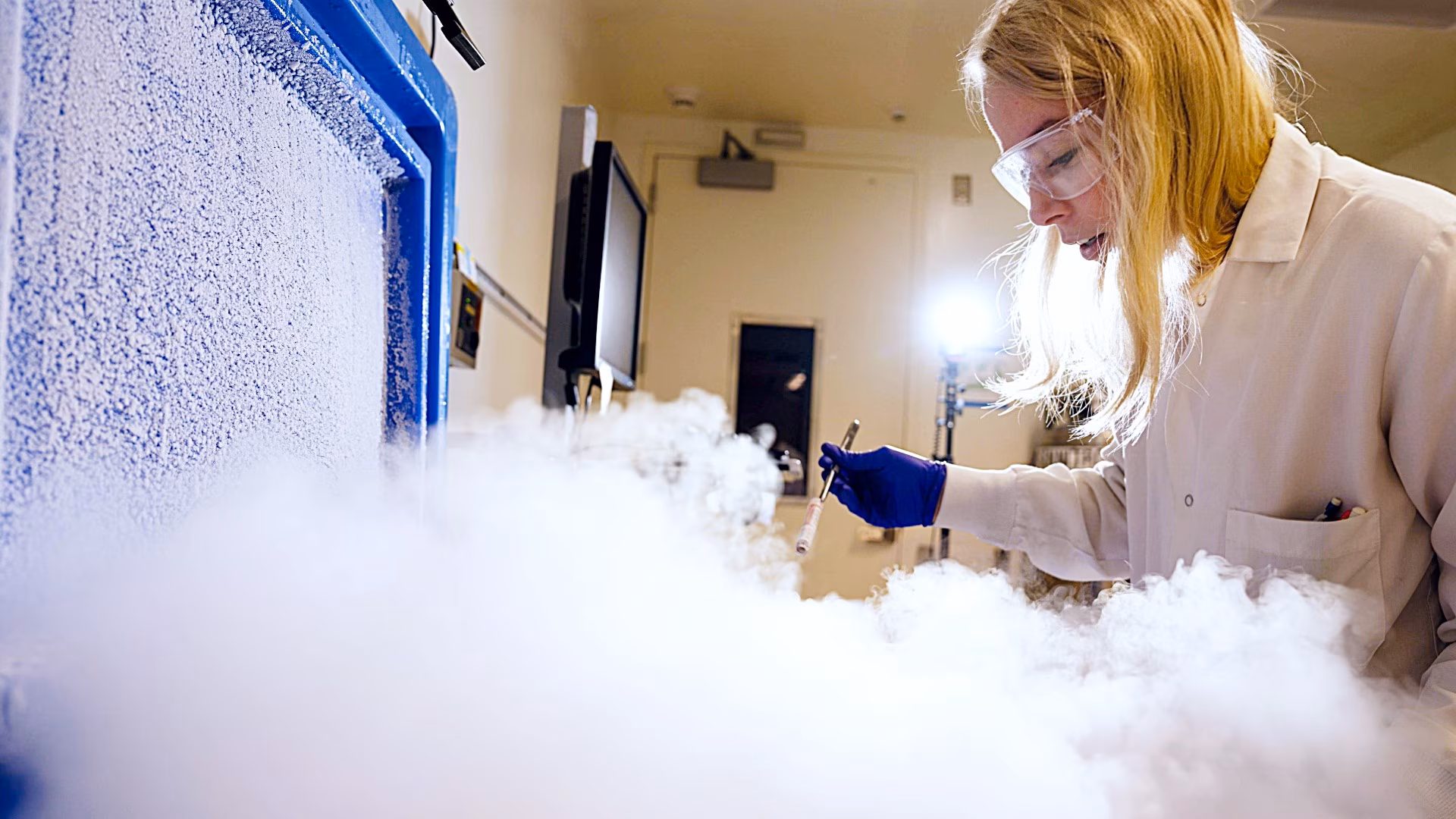 Woman scientist wearing protective eyewear handling dry ice in laboratory setting.