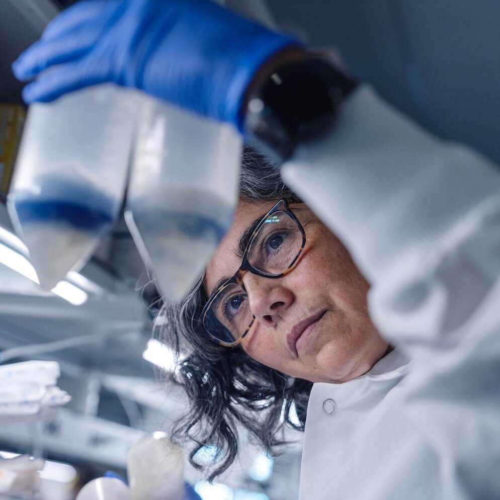 Scientist in lab coat and safety gloves examining sample with magnifying glass