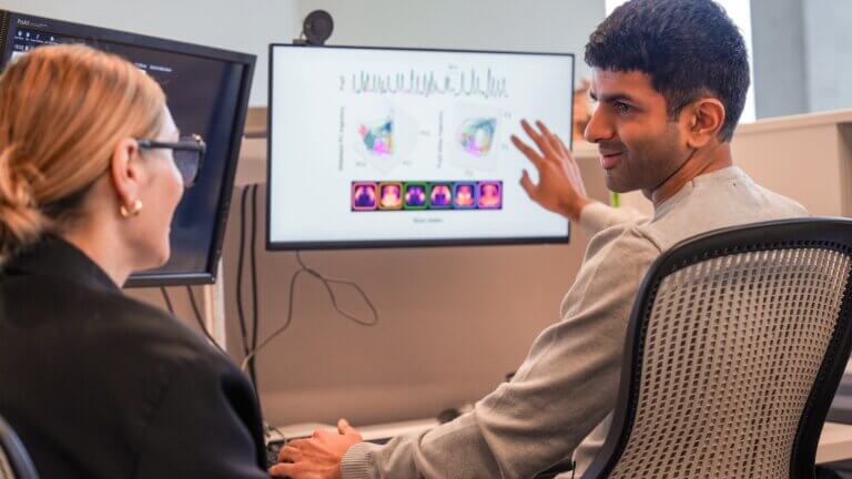 Two professionals discuss data visualizations and charts displayed on a monitor during meeting.