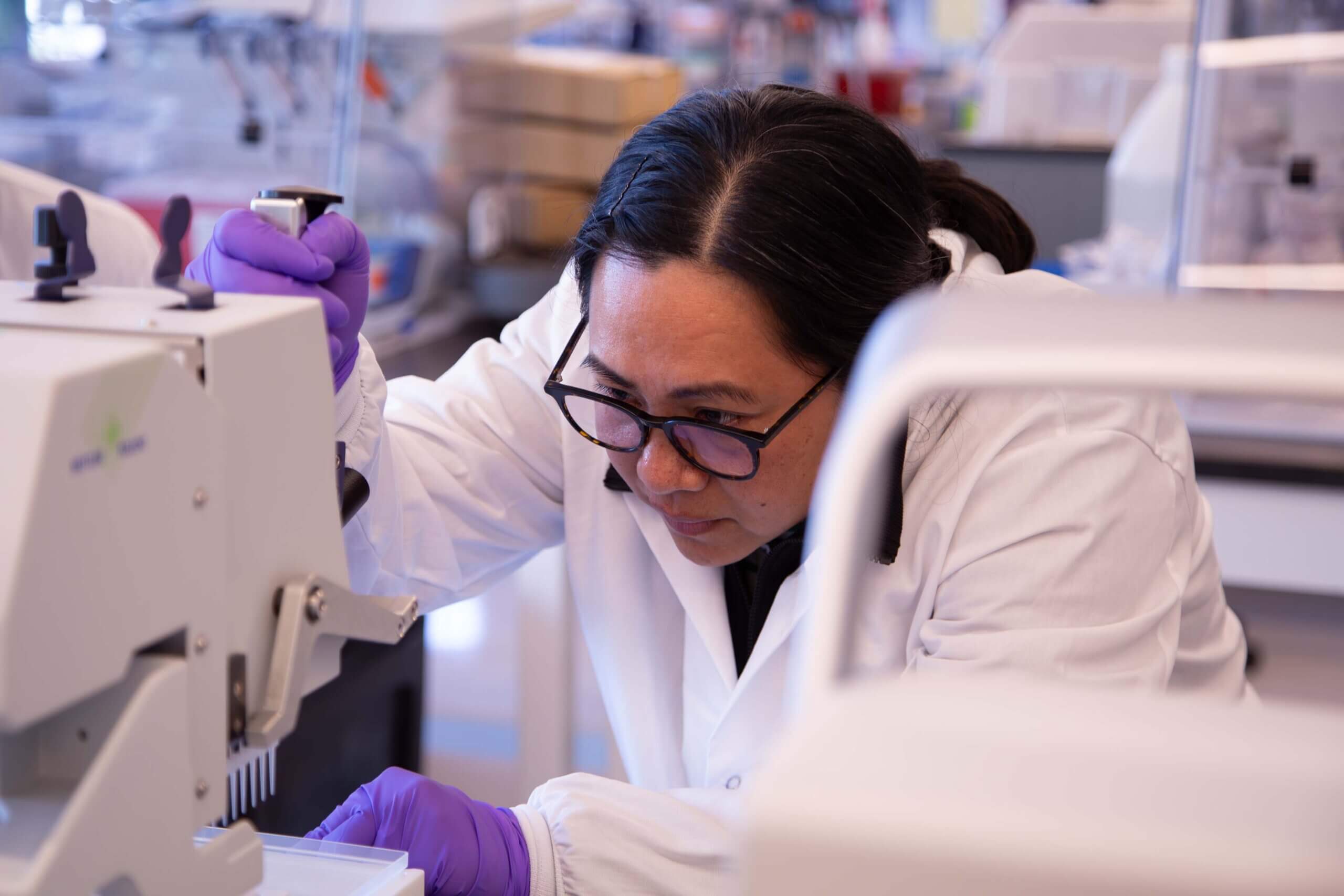 Laboratory scientist in white coat and purple gloves operating medical equipment