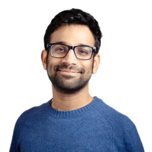 Man wearing glasses and blue sweater smiling at camera against white background