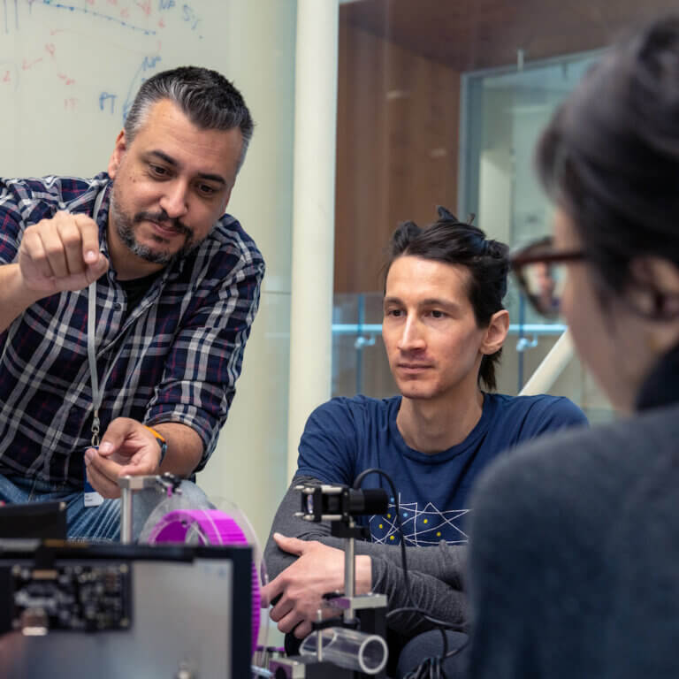 Man in checkered shirt instructs student using scientific equipment in laboratory setting.