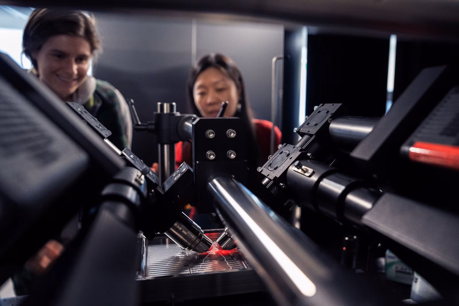 Two women examining advanced optical equipment and technology in modern laboratory setting