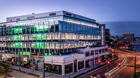 Modern glass building with green interior lighting at dusk in urban cityscape