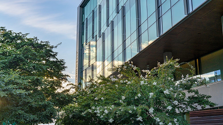 Modern glass building with overhanging concrete structure surrounded by green trees