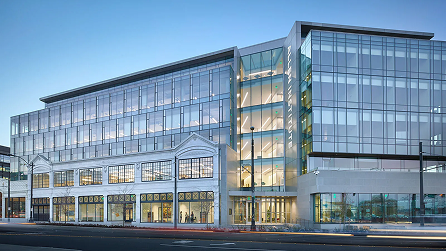 Modern multi-story glass and steel office building with illuminated interior at dusk
