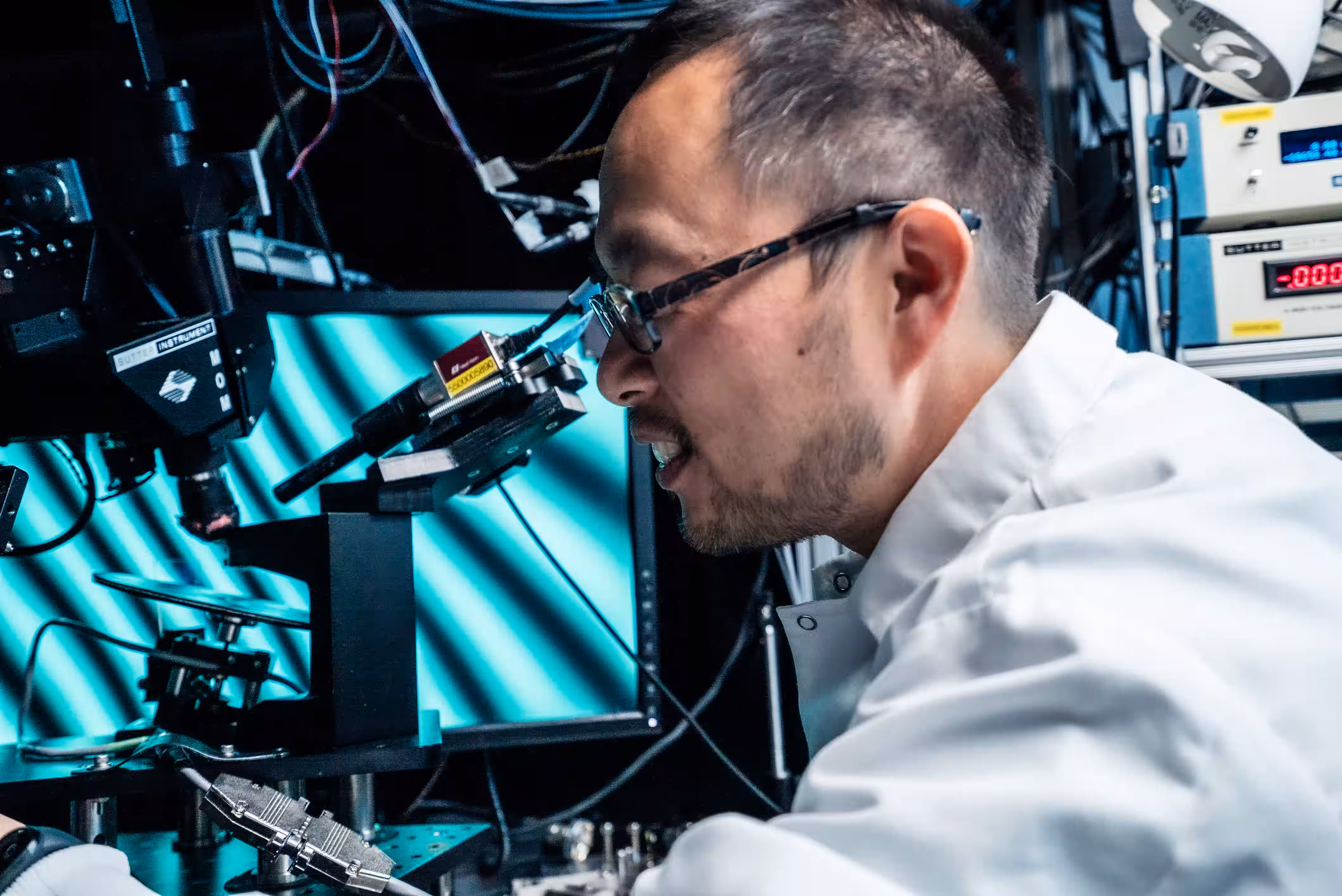 Technician in white lab coat adjusting laser equipment with cyan light and cables