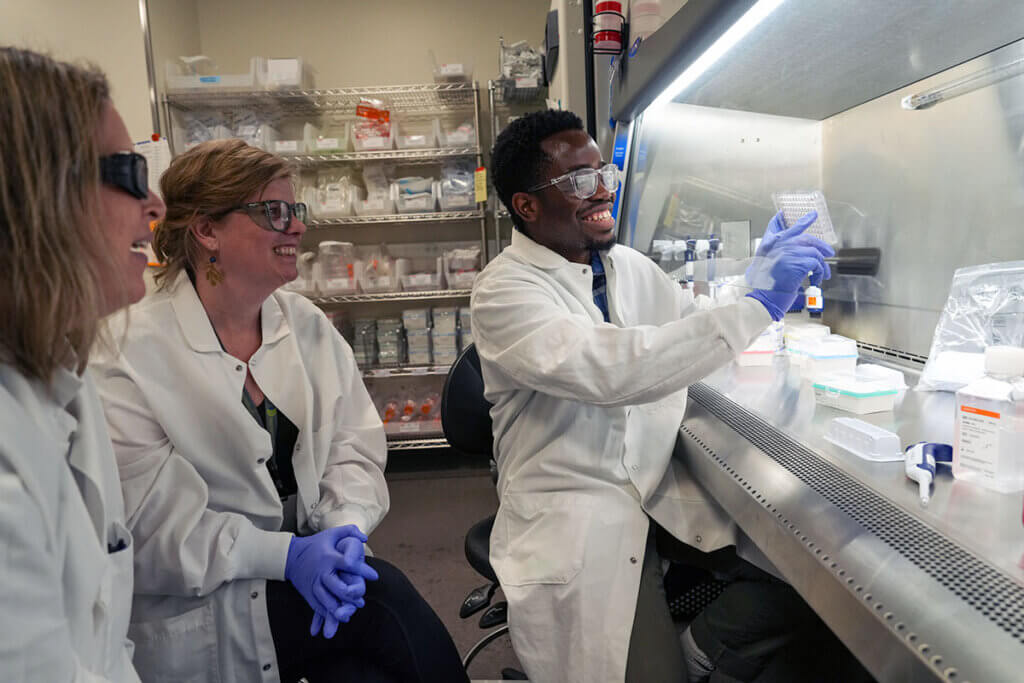 Scientists in lab coats working in biosafety cabinet with samples and equipment