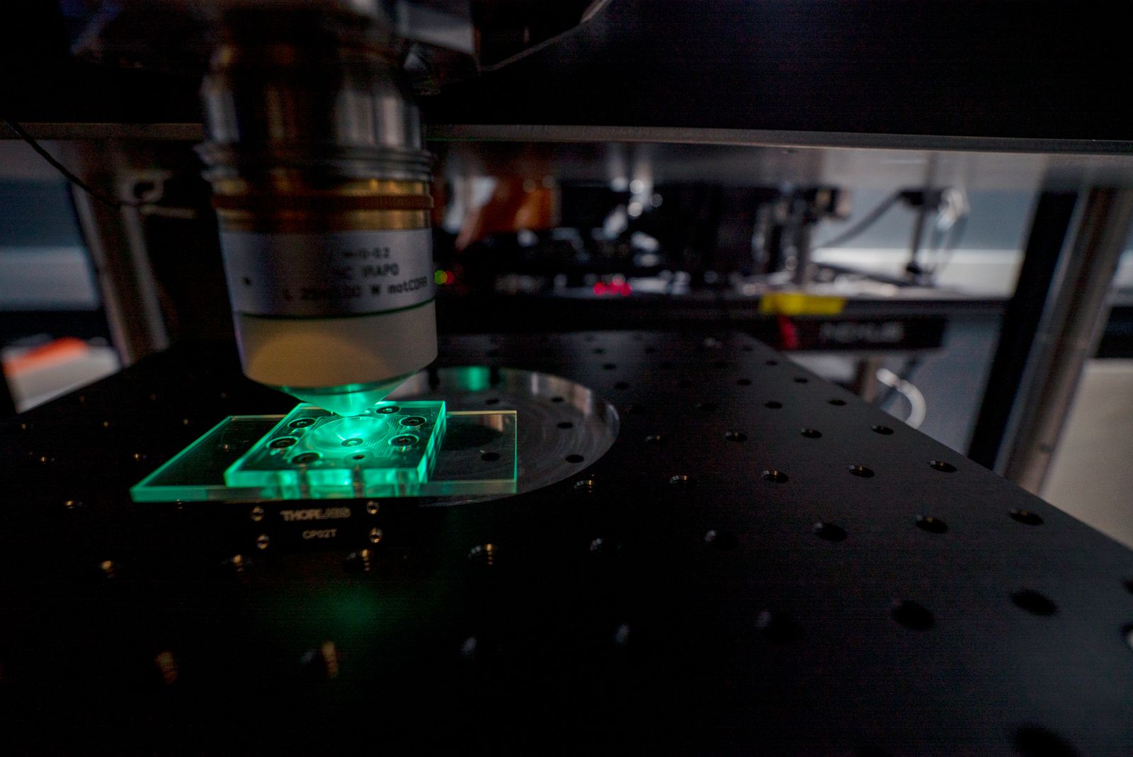 Laboratory microscope with green-lit specimen slide and optical equipment on dark surface