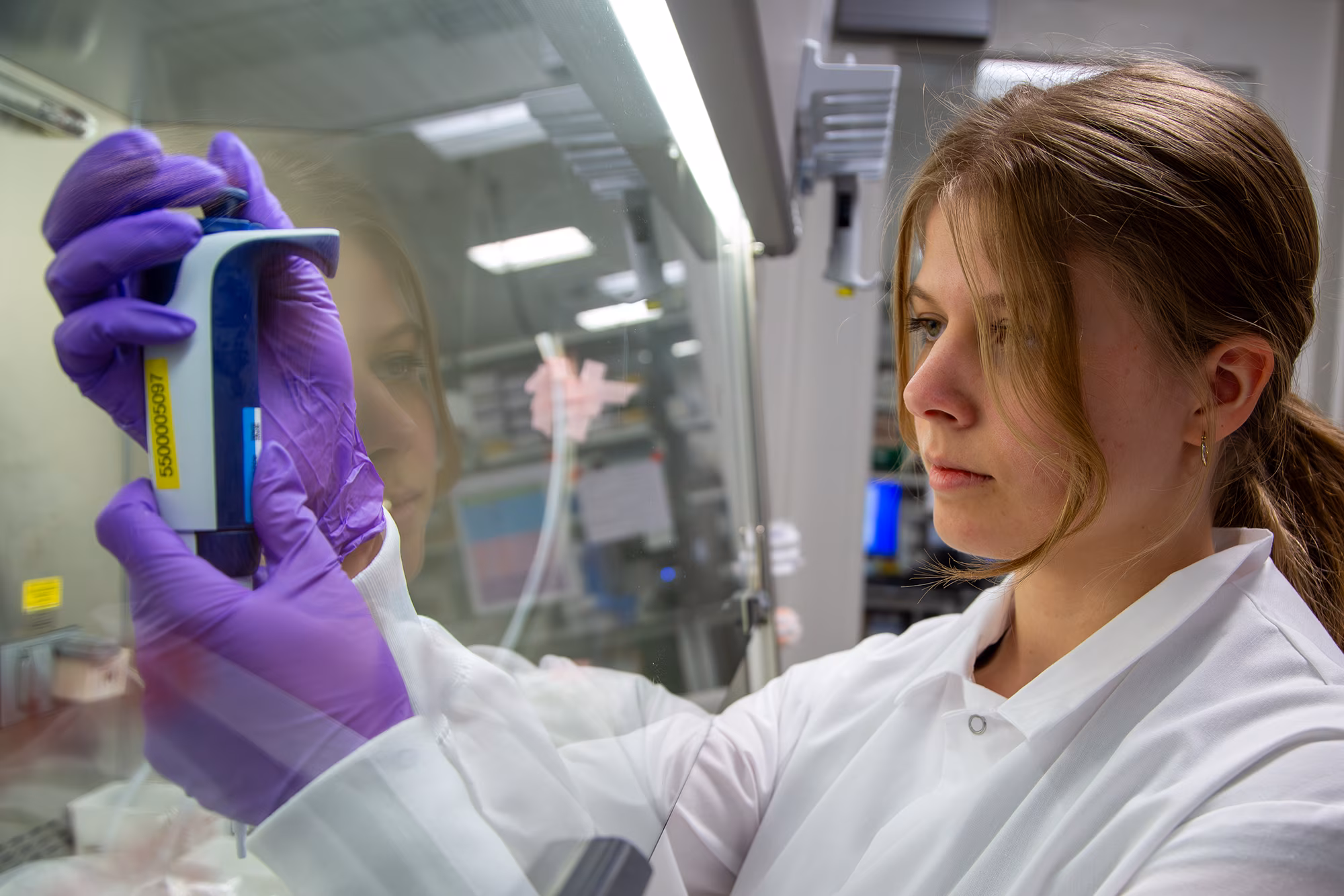 Scientist in white coat and purple gloves examining medical test tube in laboratory