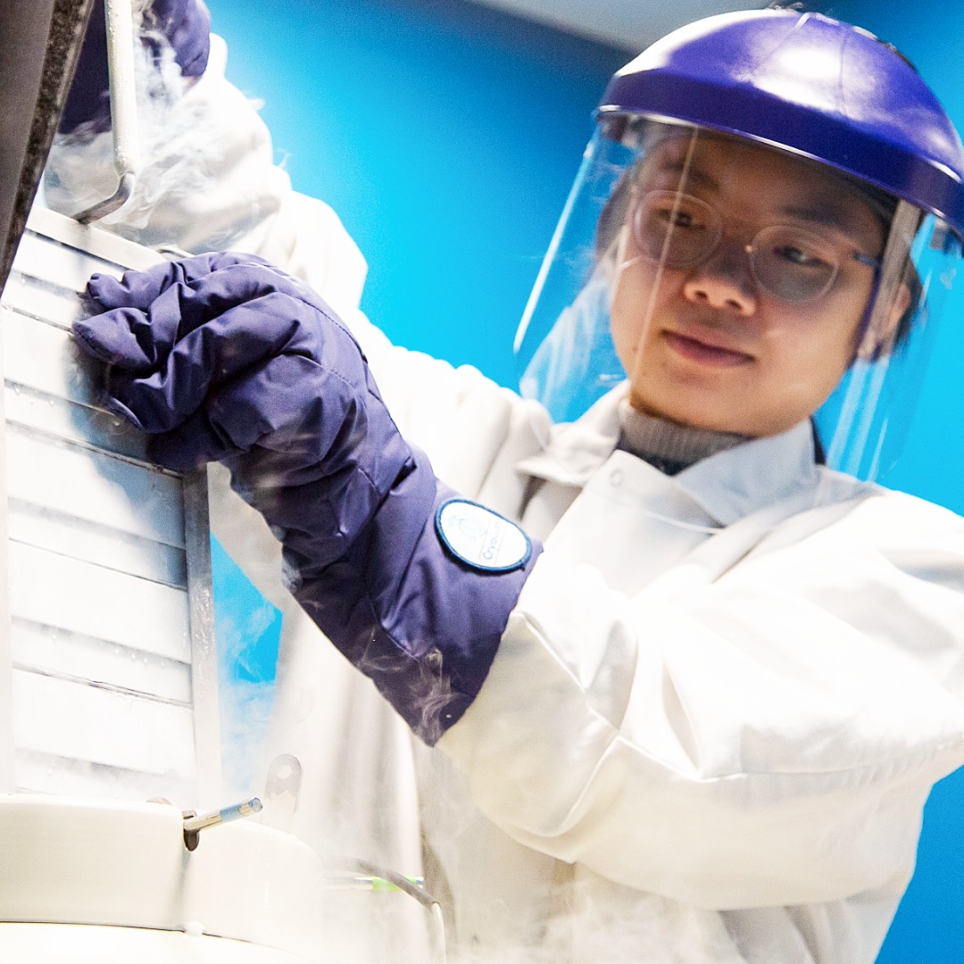 Laboratory technician in protective gear collecting sample from scientific equipment