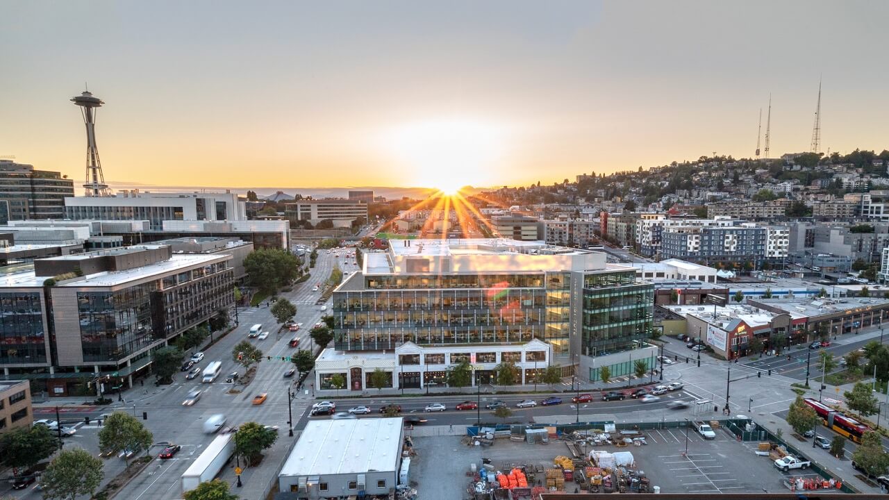 Seattle skyline featuring the Allen Institute at sunset with Space Needle, modern buildings, and street traffic visible.