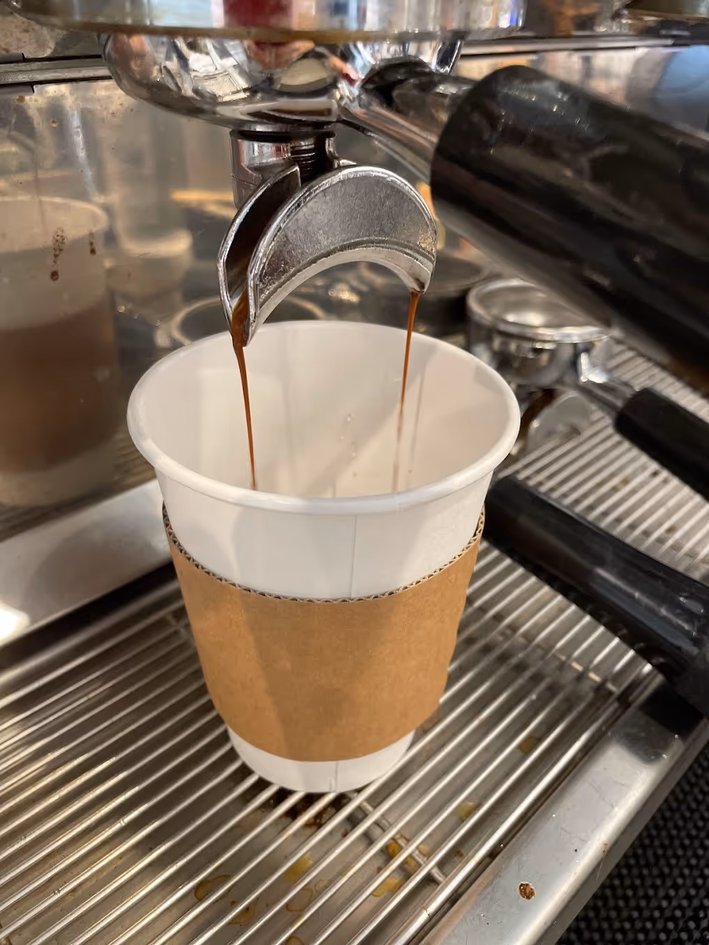 A steaming cup of coffee is being poured into a disposable paper cup.
