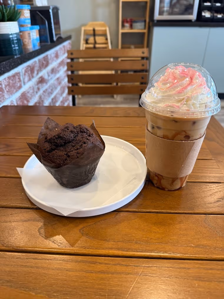 A cup of coffee beside a colorful cupcake on a wooden table, creating a cozy café atmosphere.
