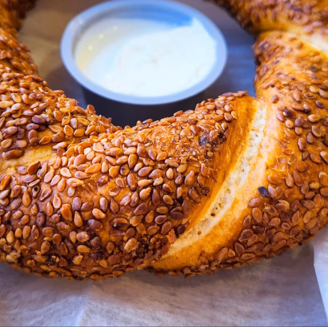 A freshly baked bagel topped with sesame seeds, served with a side of dipping sauce.