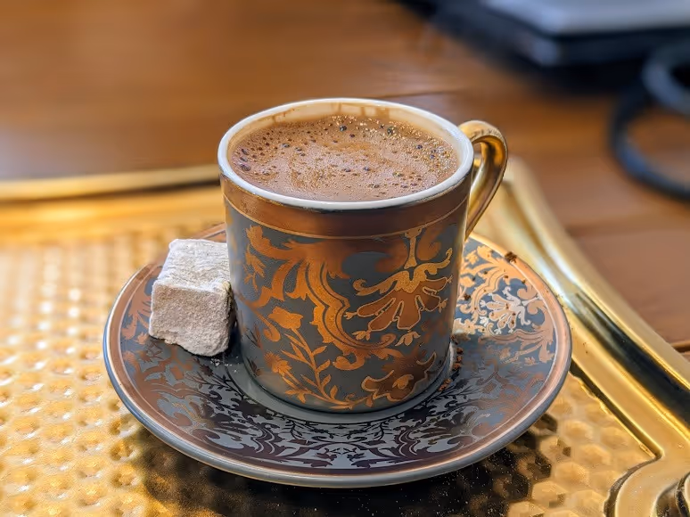 A gold cup filled with rich Turkish coffee, showcasing its dark color and frothy surface.