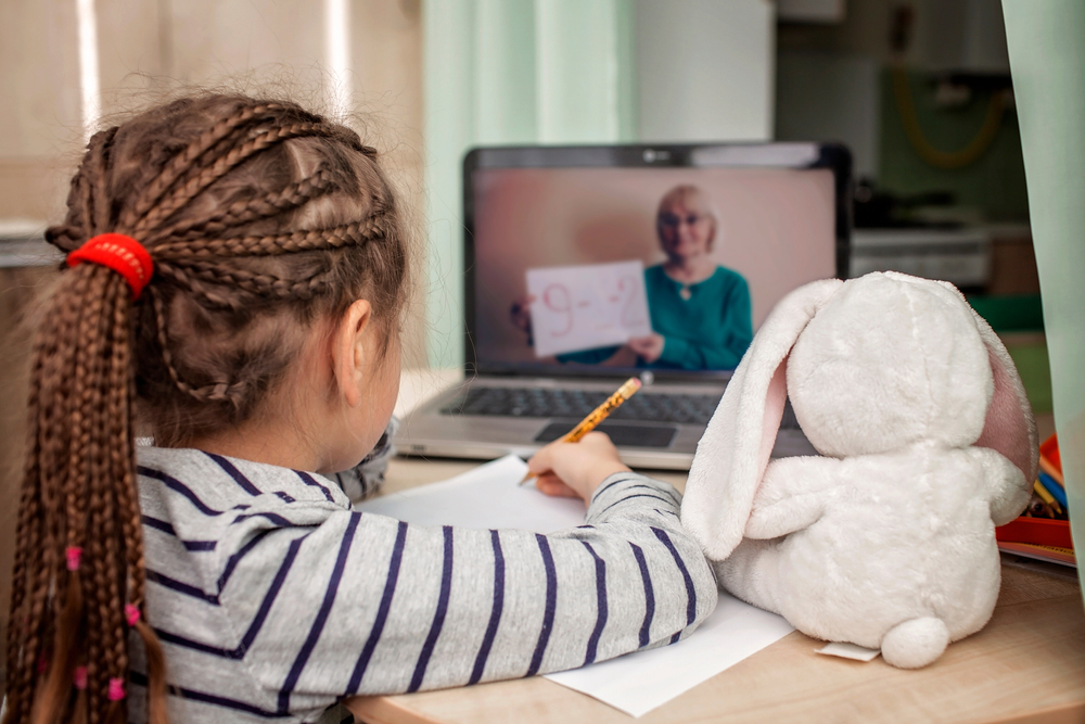 Child in online reading tutor session with laptop and plush toy