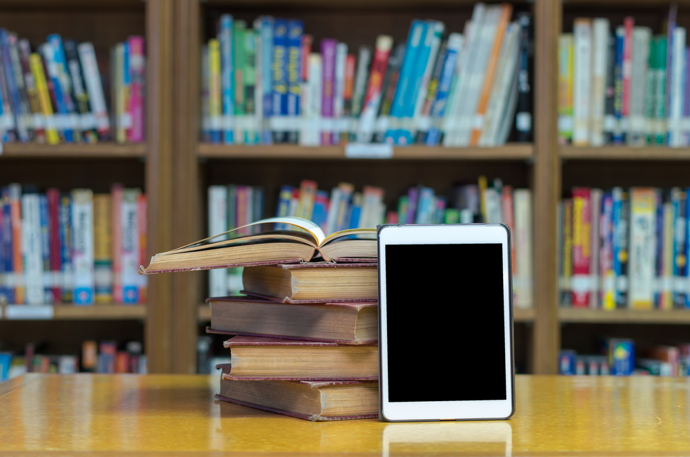 A tablet rests next to a stack of books in a library; illustration for digital library