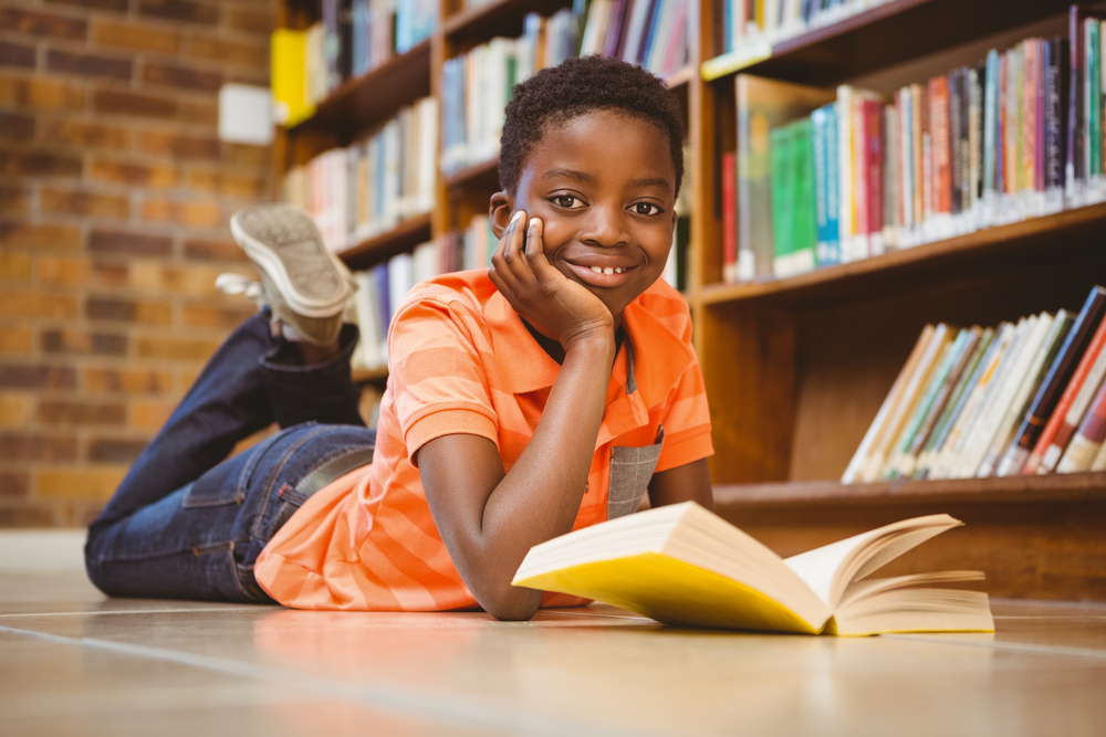 A boy reads a book on the floor of the library