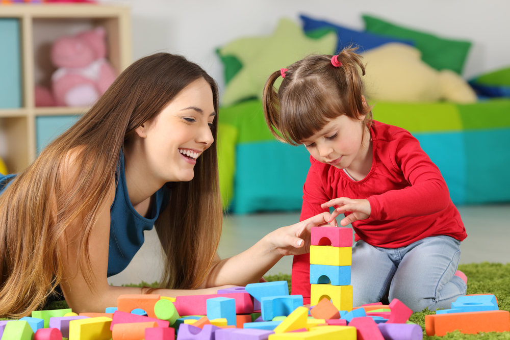 Young mother helps toddler with language learning using colorful blocks