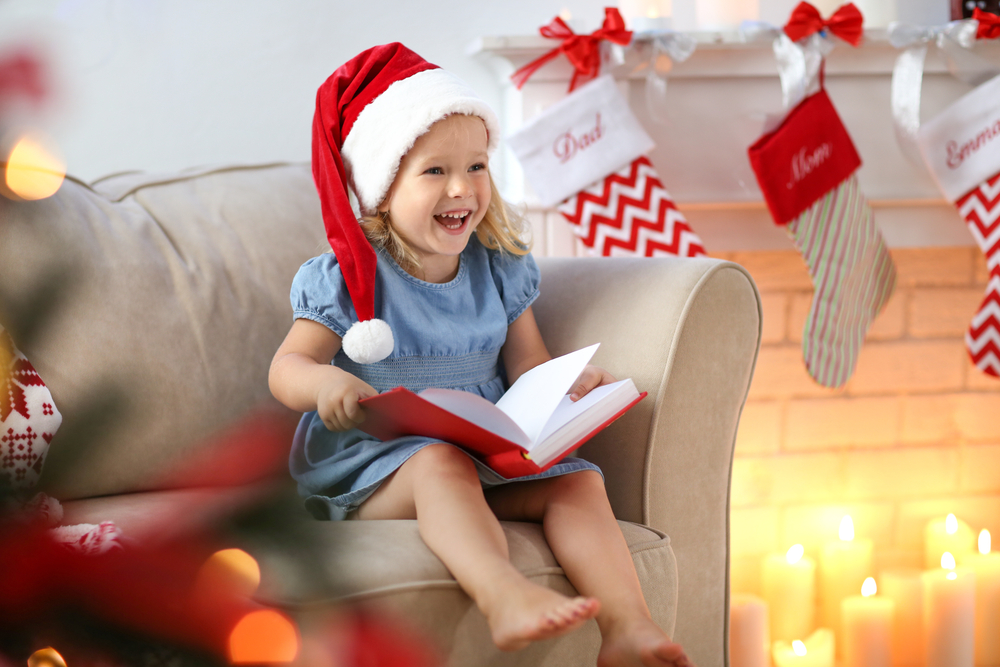 Little girl grinning while reading a book in a festive setting, highlighting the joy of 'countdown reading'