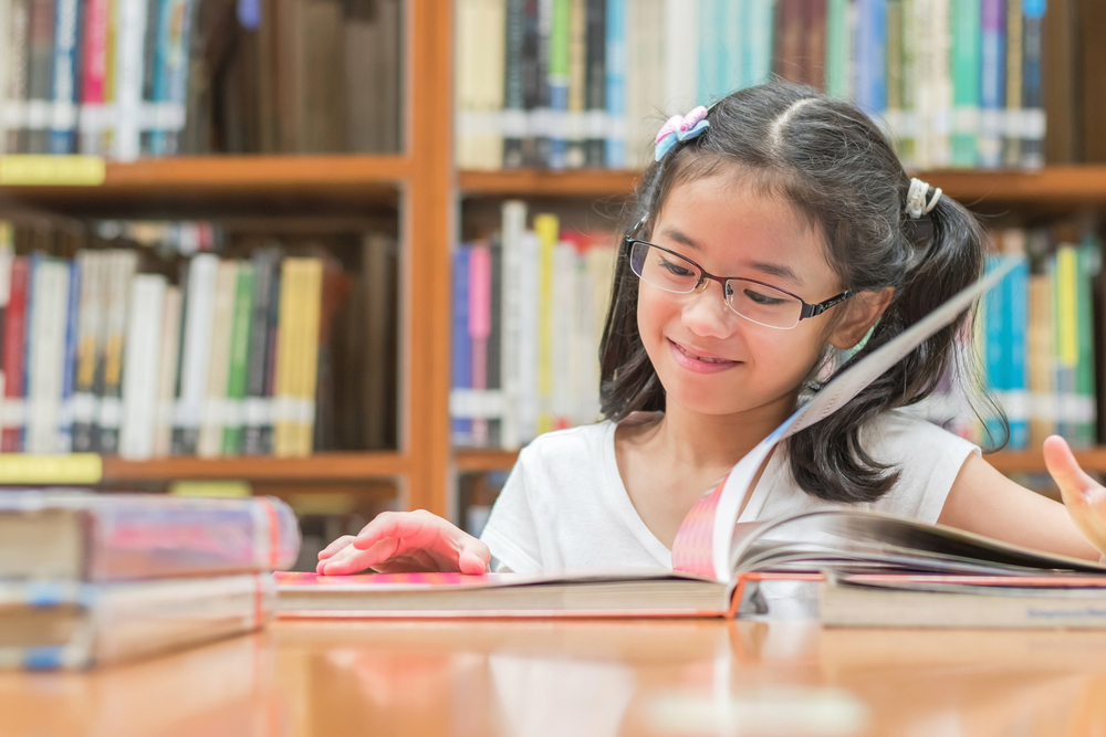 Young girl reading a book in the library, improving reading comprehension