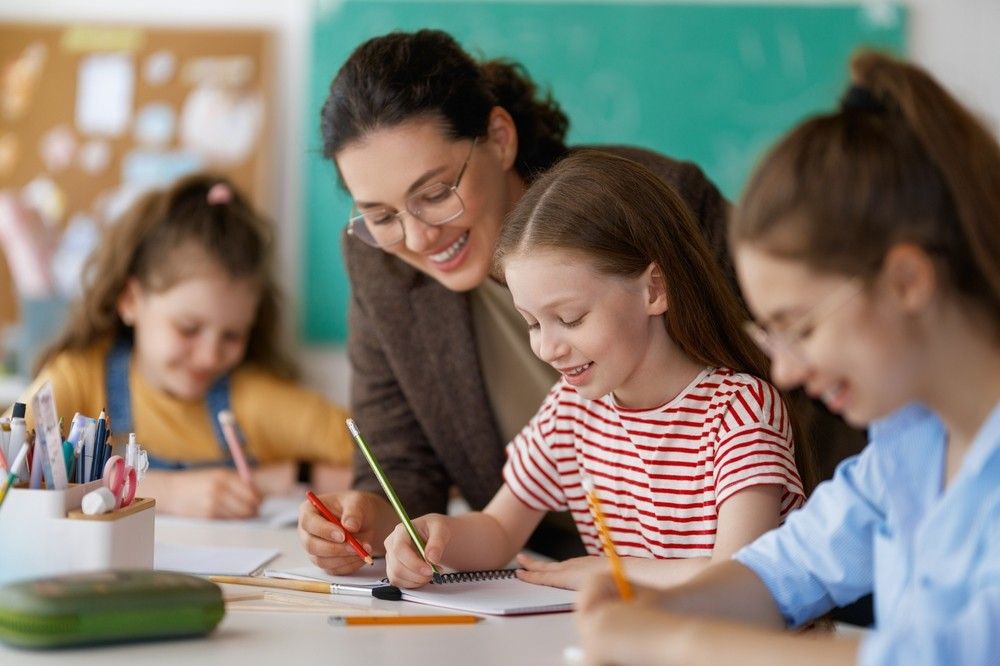 teacher helping kids to read and write in classroom