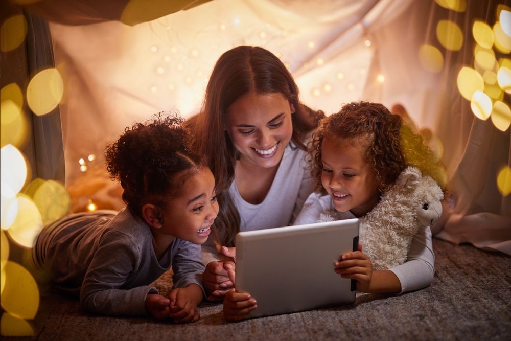 Family using an AI reading app for kids surrounded by fairy lights, exemplifying a fun assistive technology for struggling readers
