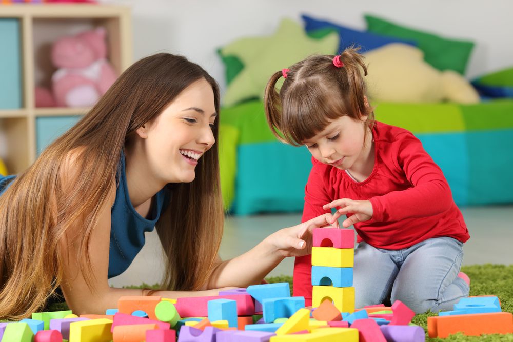 Young mother helps toddler with language learning using colorful blocks