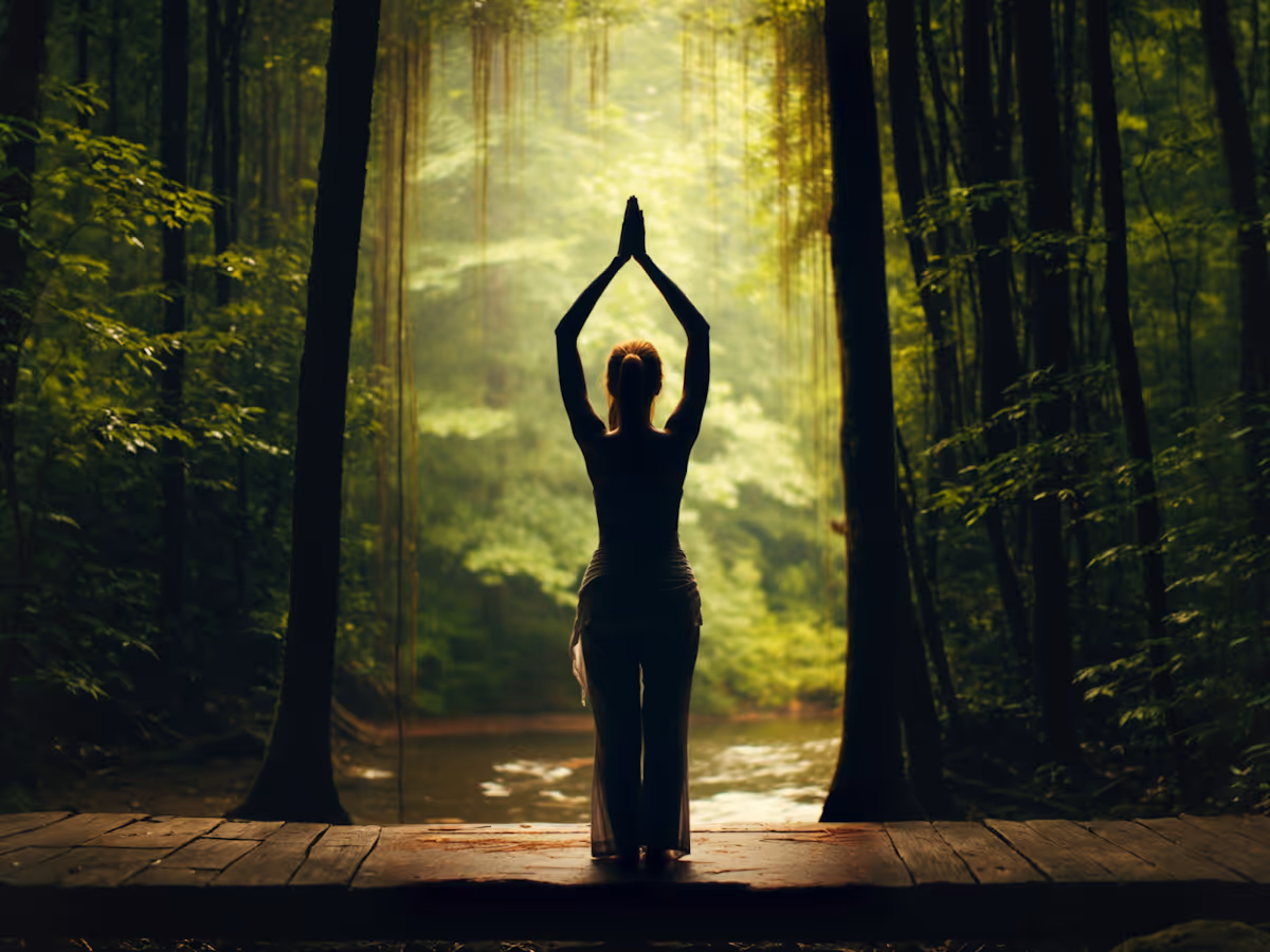 Person practicing yoga with hands raised above head on a wooden platform in a lush green forest.
