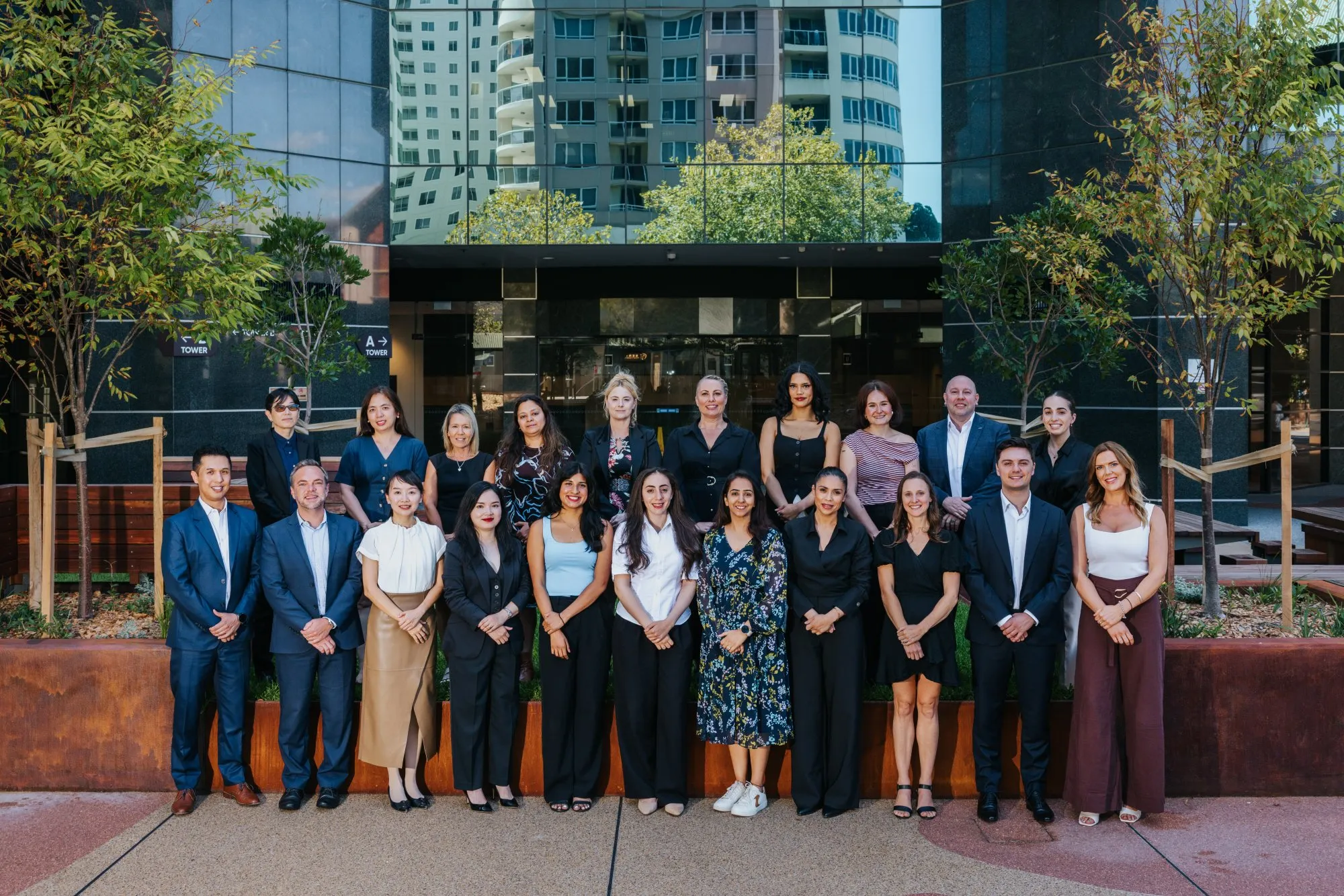 Group of diverse professionals posing outside a modern office building with glass windows and trees.