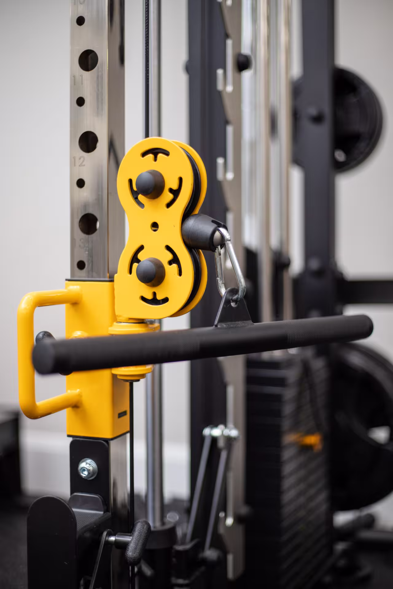 Close-up of yellow pulley system with black handle on a cable machine in a gym.
