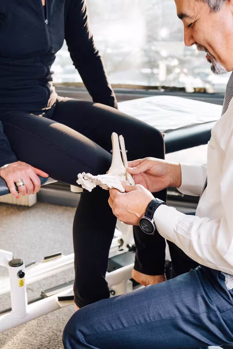 Medical professional showing a foot bone model to a seated person dressed in black activewear.