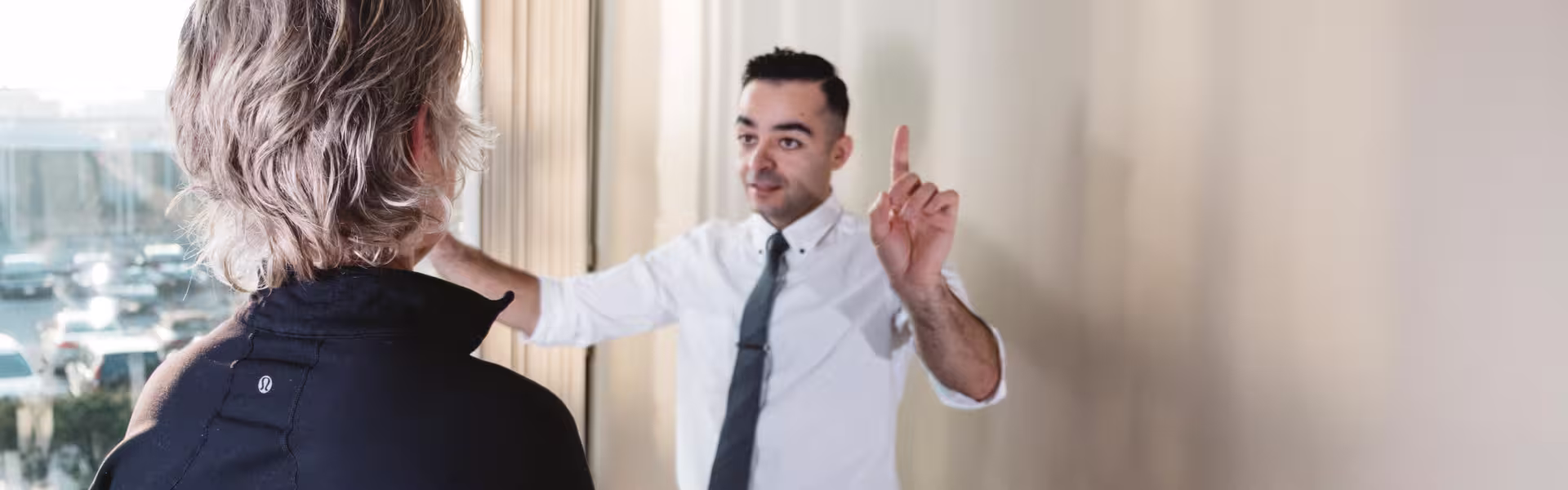 Businessman in white shirt and tie speaking and gesturing with raised finger to a person with blonde hair wearing a black jacket.