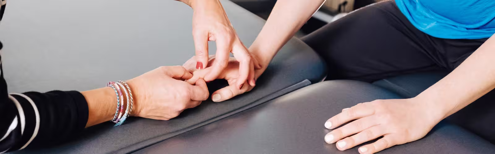 Therapist's hands performing hand acupuncture or acupressure on a patient's finger on a gray therapy table.