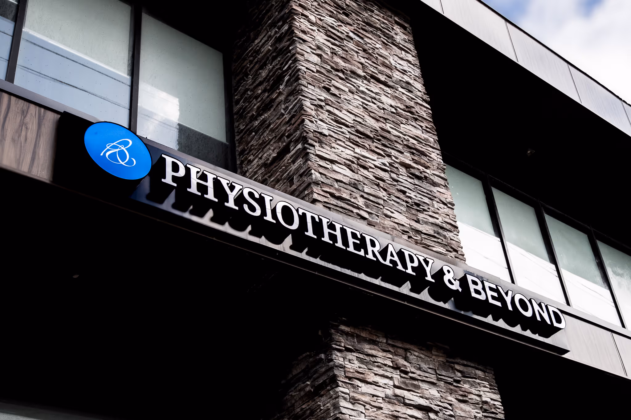 Sign reading 'Physiotherapy & Beyond' on a modern stone and glass building.