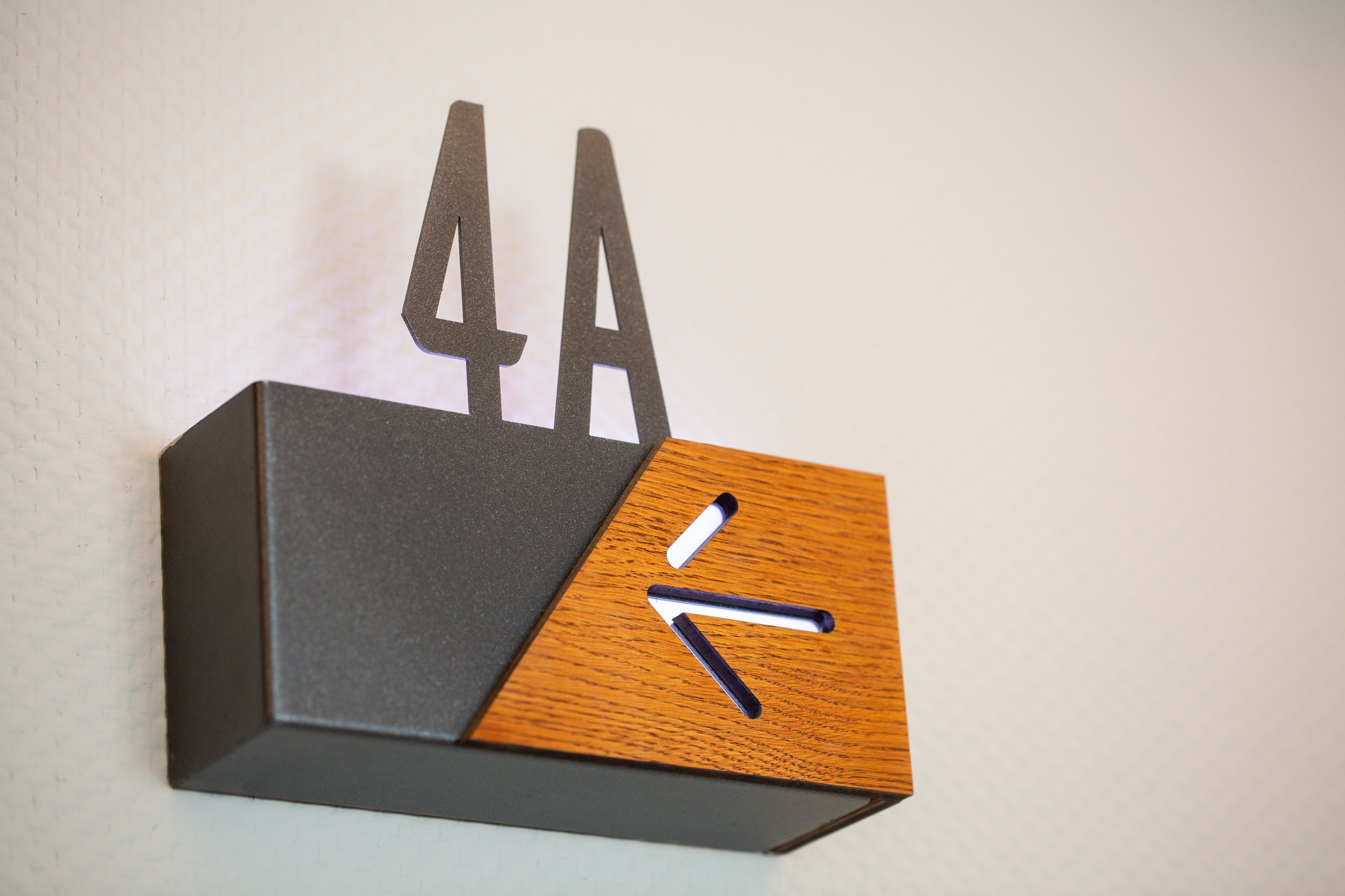 Modern room number sign 4A with a wooden arrow pointing left attached to a light-colored textured wall.