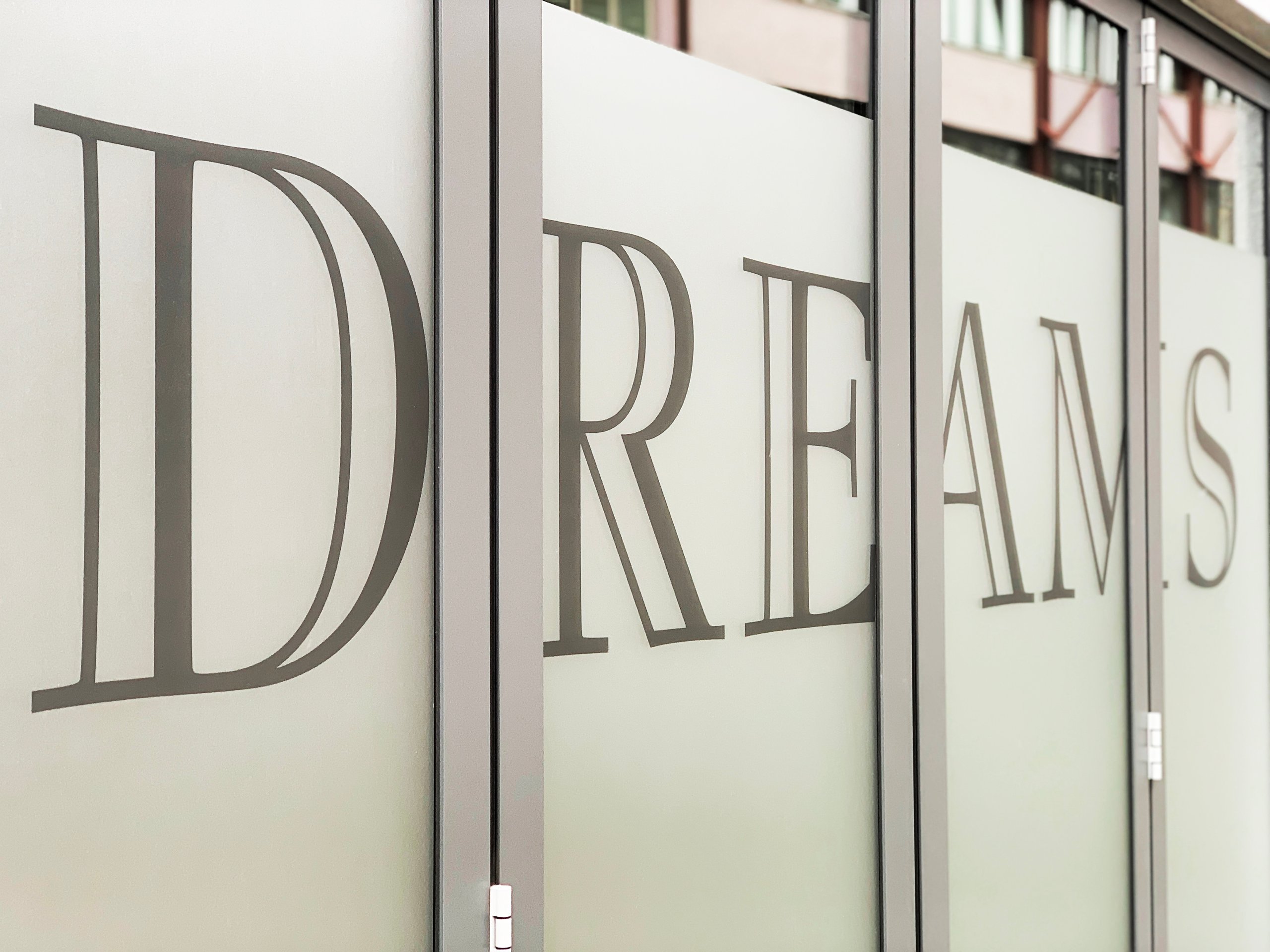Large letters spelling the word DREAMS on frosted glass panels of an office or storefront.