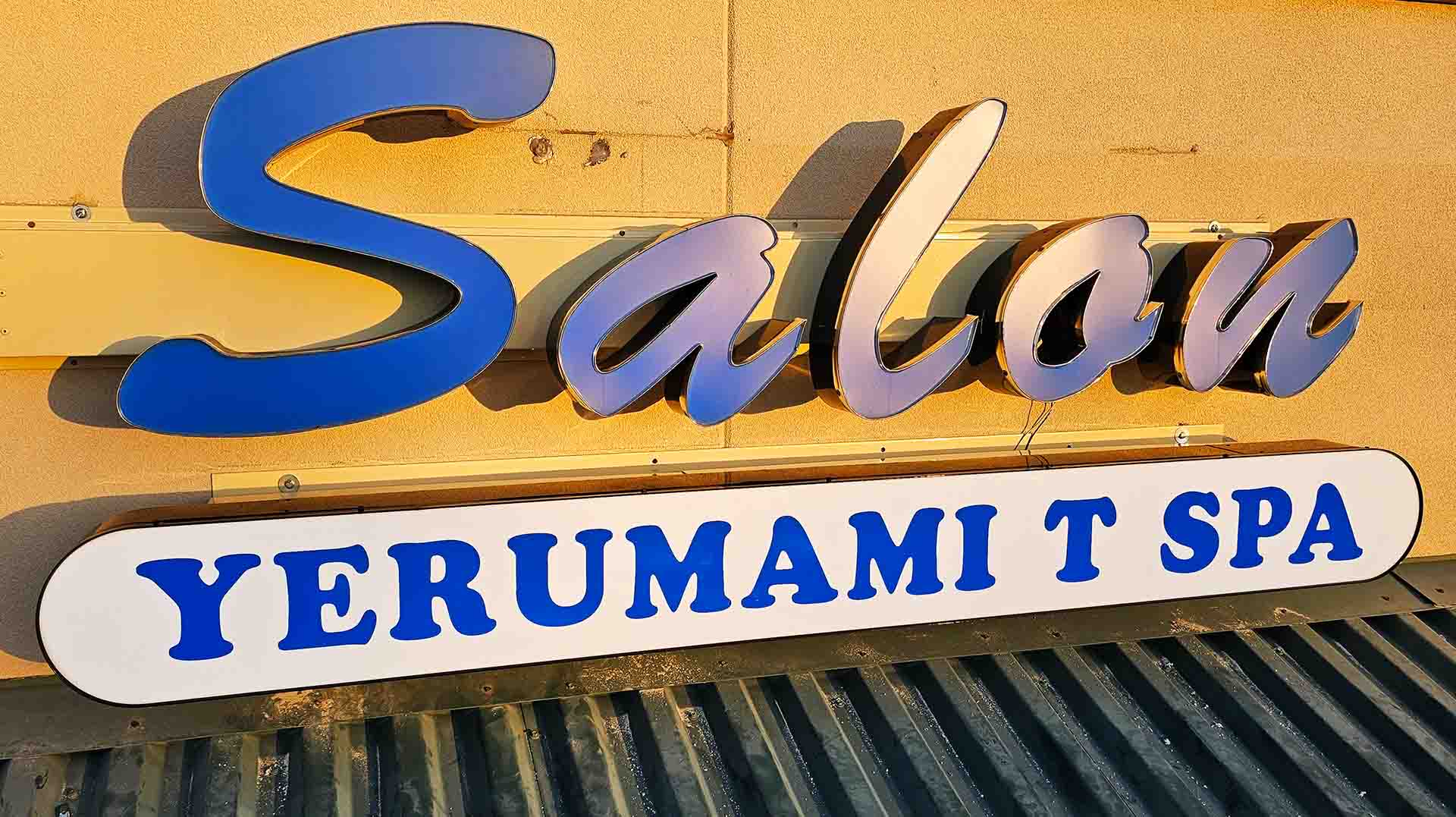 Sign on a building wall reading 'Saloon YERUMAMI T SPA' with blue and white letters.