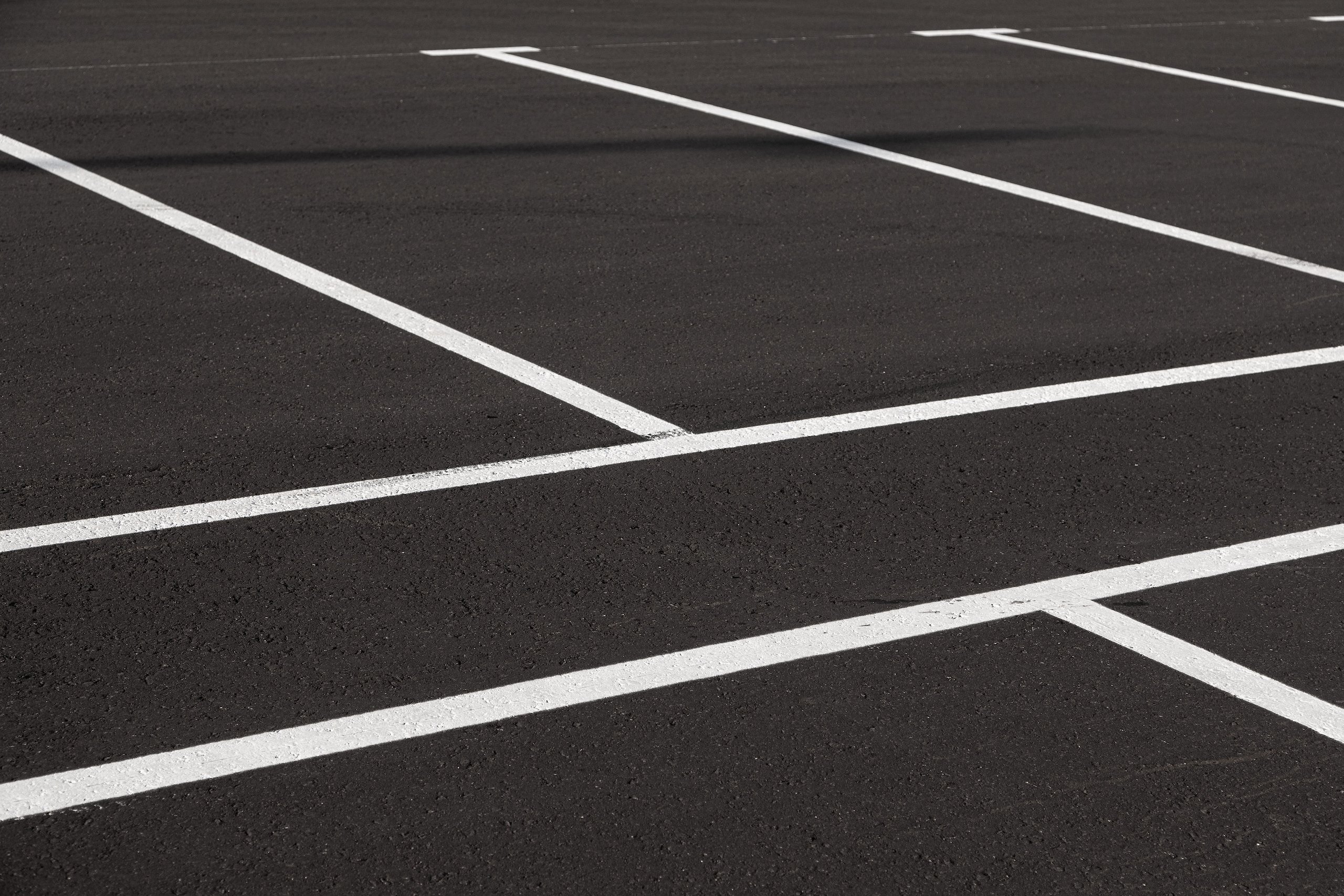 Empty asphalt parking lot with clearly marked white parking space lines.