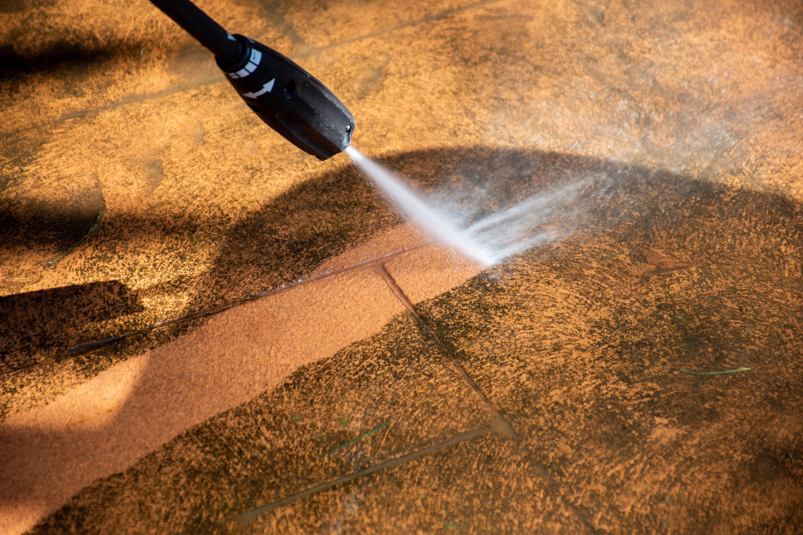 Pressure washer nozzle spraying water to clean dirt off a concrete surface.